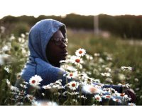 Older boy with grey sweatshirt hood on sitting in a field of daisies