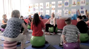 A group of students and adults sit on bouncing balls in a classroom.
