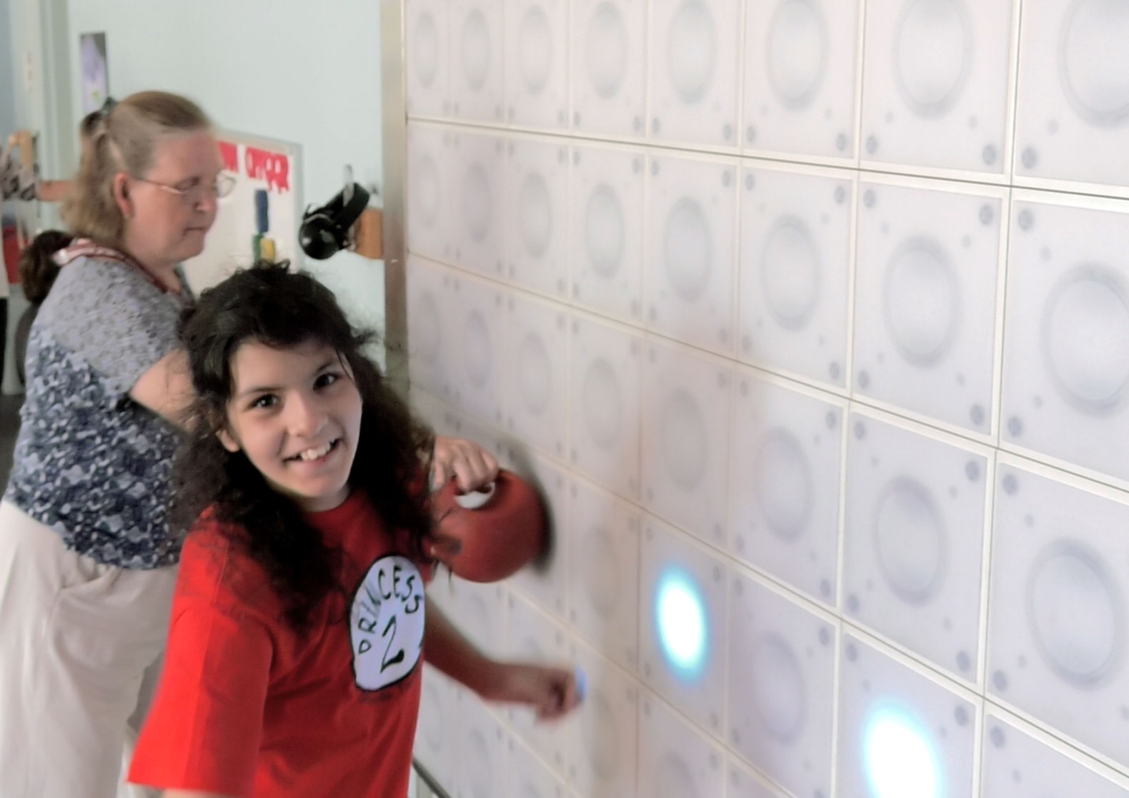 A girl taps different squares on a wall as they light up.