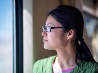 A side shot of a young female teacher in glasses and a green shirt looking out of a window. 