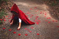 Young girl in a red velvet hooded cape, picking flower petals off the ground
