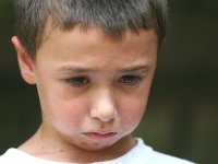 A closeup of a young boy with his head down, tears trickling down his cheeks. 