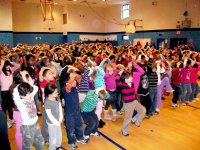 The basketball court is filled with elementary school kids standing next to each other, filling the whole court, with their hands on their heads.