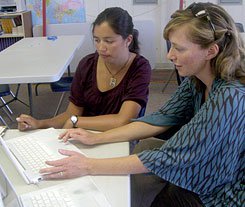 Two women sitting next to each other at a desk working on a laptop