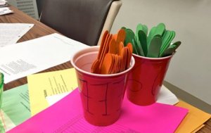 Orange and green popsicle sticks in red plastic cups on a teacher's desk