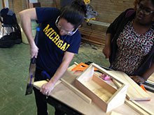 A photo of a girl sawing wood for her project.