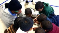 Teacher on the floor surrounded by working students