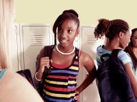 Four female students are standing in a hallway beside their lockers, talking to each other in pairs.