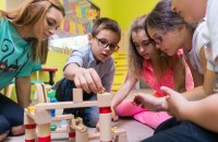 View of a teacher helping children with the construction of a wooden train circuit during supervised free playtime