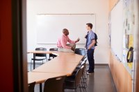 A teacher and a student talking after class, smiling and looking relaxed