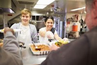 Two students serving free meals to homeless people at a free dining room