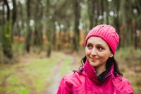 A woman walking through the woods in a pink rain jacket and knit hat