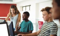 A group of middle school students using desktop computers and engaging with each other