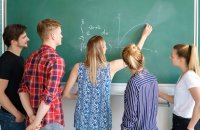 A group of students watching a teacher draw a graph on a blackboard.