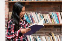 A student reading a book in front of a bookshelf