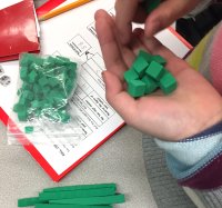 A child's hand holding green base ten blocks for a math game