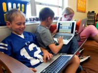 Three kids sitting in class on a big futon each with a laptop