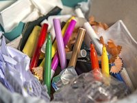 A photo of a classroom garbage can, with wadded up papers, pencils, and markers.