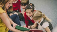 A teacher shares a book with young students.