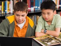 Two boys looking at a laptop and open book