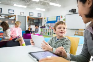 Teacher and elementary student using digital tablets in classroom.