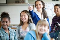 Teacher pointing at board while a group of smiling middle school students look on.