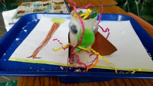 A student-made model of a fictitious animal made from pipe cleaners, a cardboard tube, googly eyes, and pom poms