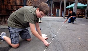 Two boys using measuring tape and chalk on the school grounds