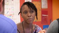 A close up of a female teacher from the shoulders up. She's sitting at a table with two other teachers, talking.