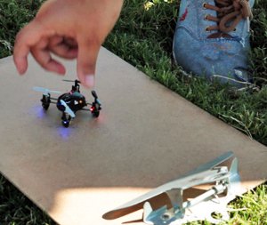 Close up of a kid's hand reaching for a small drone which is sitting on a clipboard on the grass 
