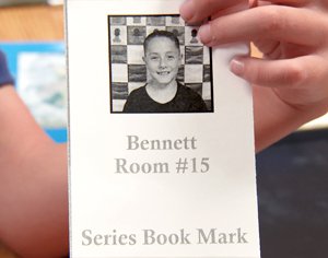 Boy holding his Series Book Mark that shows his picture, name, and room number