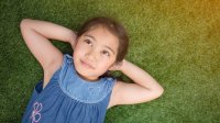 A young girl lies on her back, relaxing on the grass.