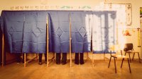 A row of voting machines in a classroom, with people inside voting