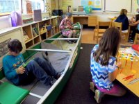 Kids working independently sitting in a canoe, and in groups at a small round table and a square table at floor height