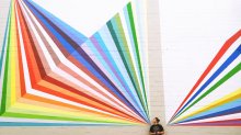 Girl standing in front of an outdoor mural of rainbow rays.