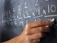 Hand holding chalk writing multiplication problems on a blackboard