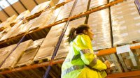 A young woman checks boxes in a storeroom.