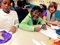 Three elementary school children sitting together at a table in class coloring with markers