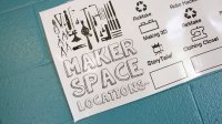 A poster on a blue-painted brick wall that says, "Maker Space Locations" on the left, and on the right of the poster it shows Monday through Friday and three maker spaces beneath each day, like "ReMake," "Making 3D," and StoryTeller."