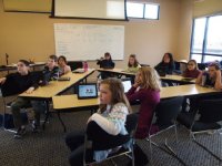 Ten students are sitting in a classroom at rectangular tables positioned in a triangle, all looking up in the same direction. 