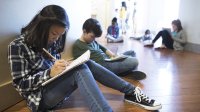 Students work independently while sitting in a school hallway.