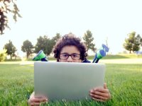 Boy laying on the lawn peeking out over his laptop