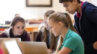 Three school students crowded around a computer.