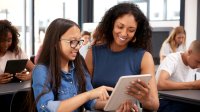 A female teacher and twelve-year-old girl are standing, smiling, and looking at a daily planner together.