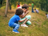 Two girls sitting next to each other looking closely at long skinny sticks