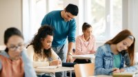 High school teacher works with a student at her desk