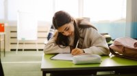 Middle school student writing in a notebook at her desk