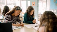 Three middle school students writing and working together at a table in the classroom