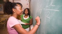 Two middle school students working on a math problem at a chalkboard