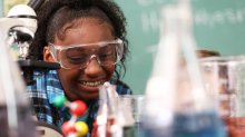 Photo of a smiling student wearing protective eyewear in science class with beakers in foreground
